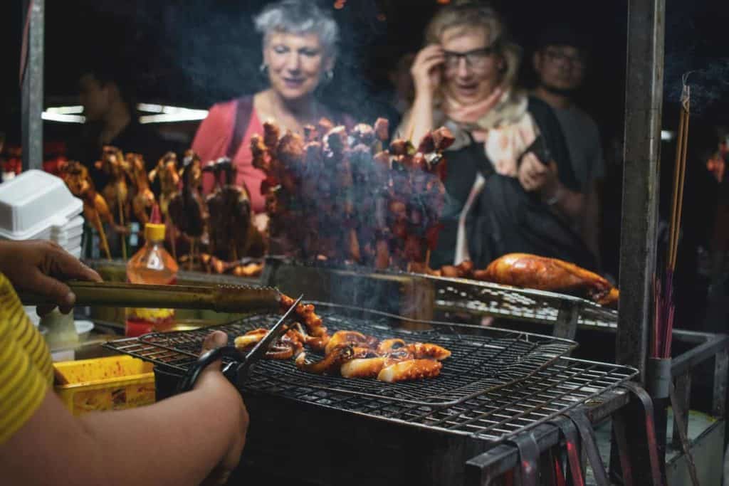 Két nő áll a grillezett hús előtt. A rosszul elkészített hús lehet az egyik fő oka a nyaralás alatti hasmenésnek